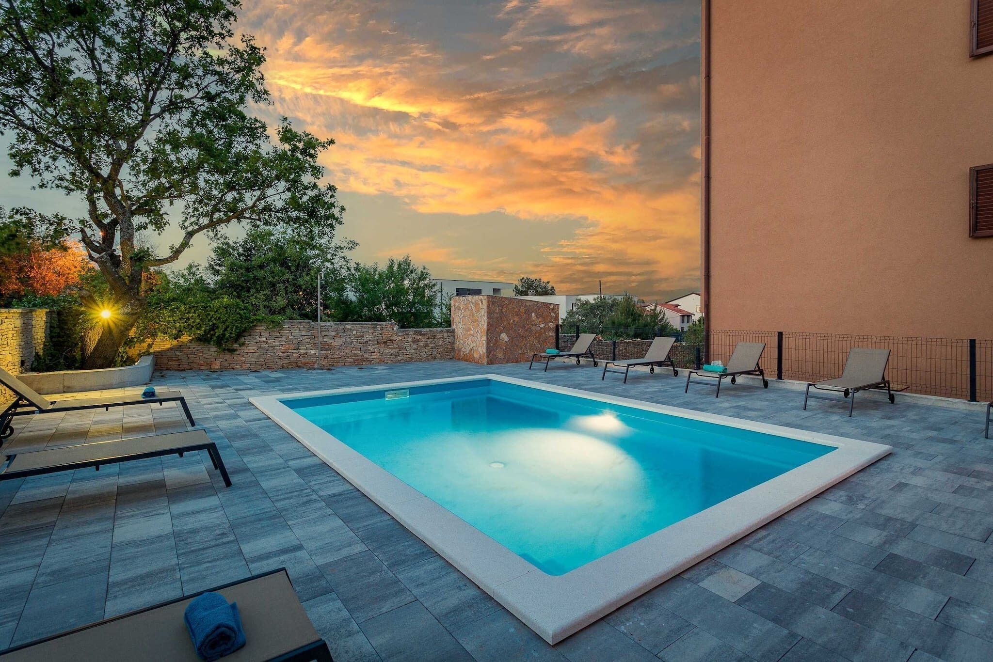 Una piscina rectangular amb una terrassa enrajolada, rodejada de gandules i una paret de pedra.