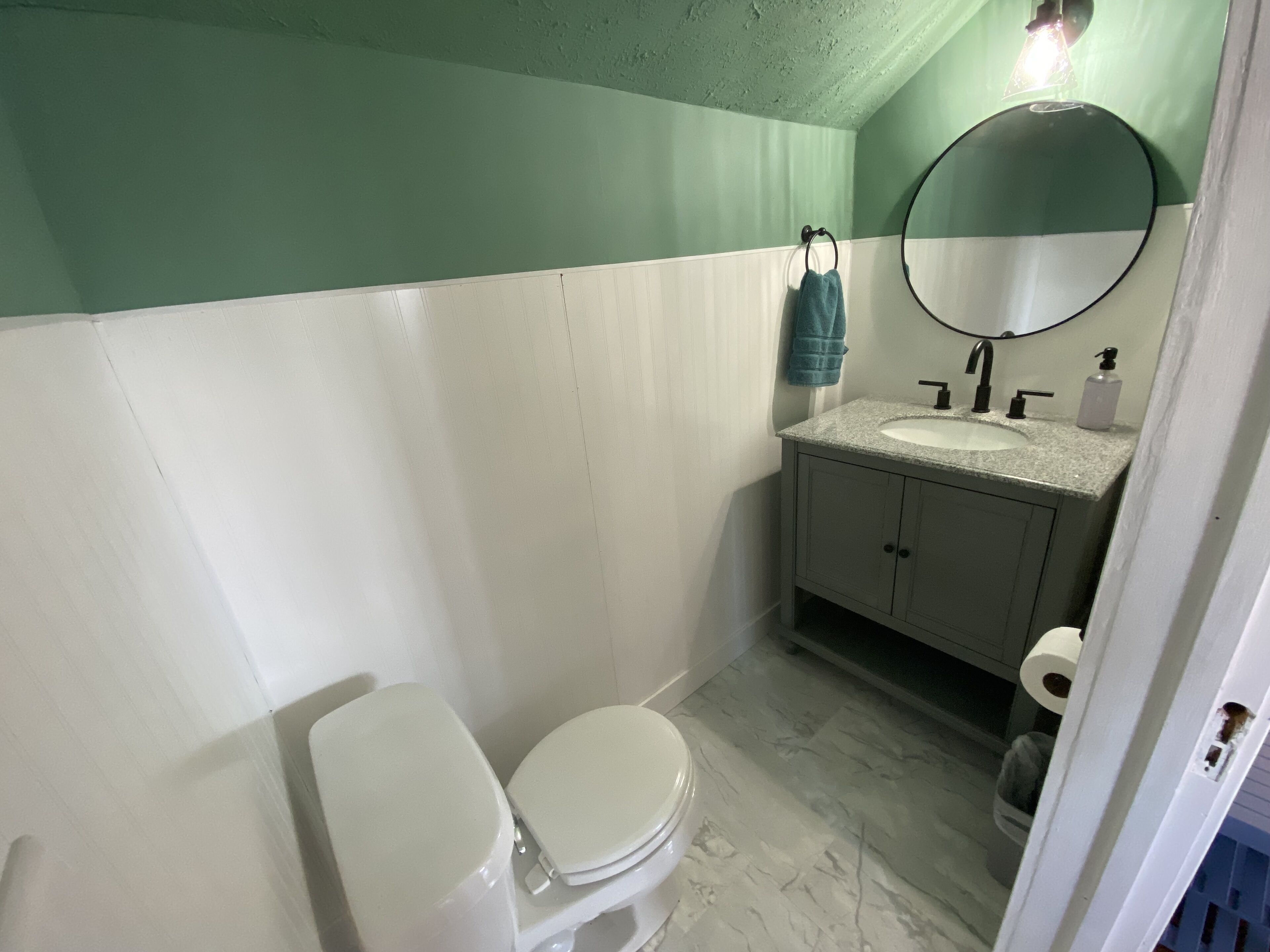 A bathroom with a white toilet, a sink with a mirror above it, and a towel hanging on the wall.