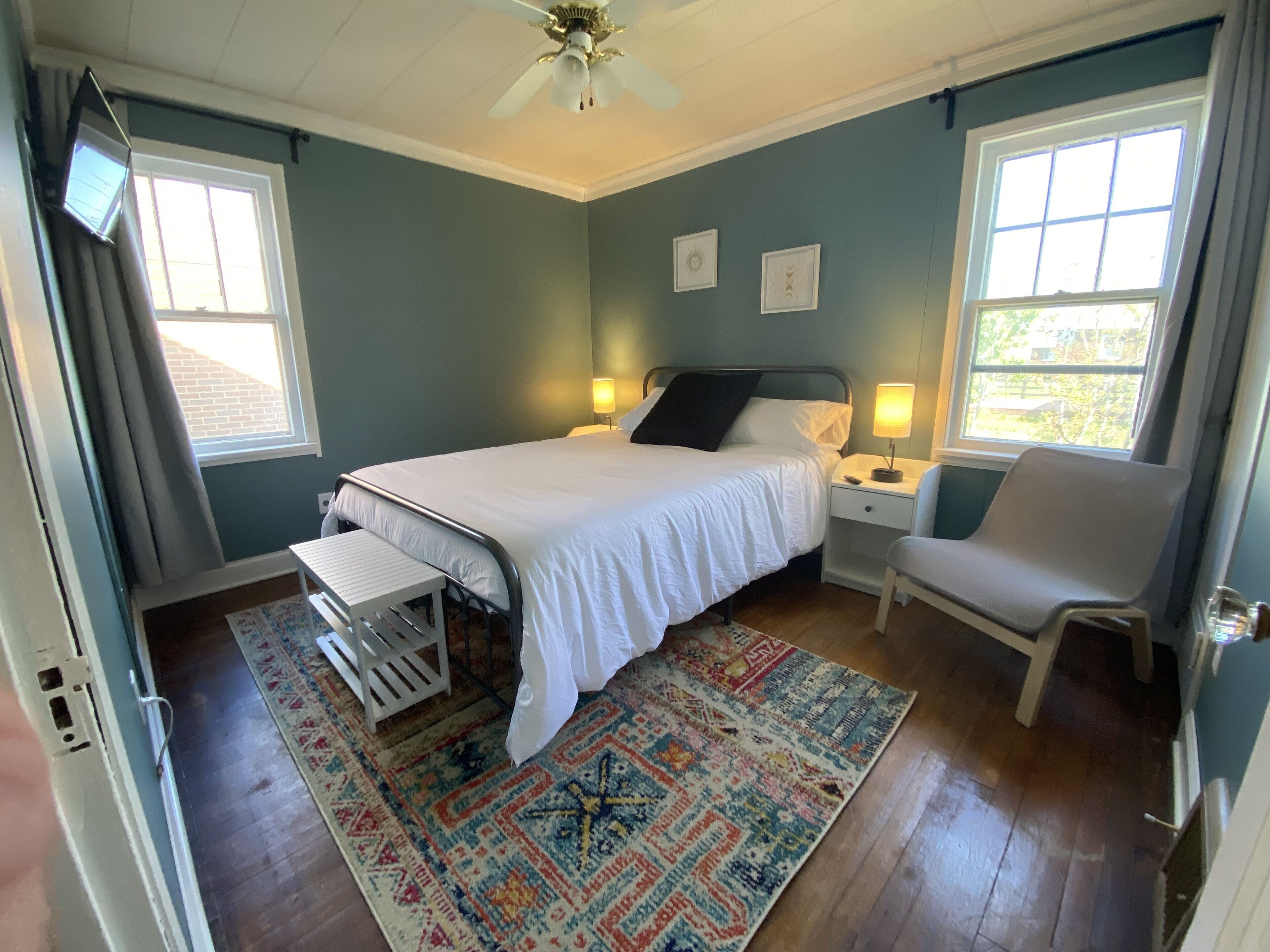 A bedroom with a bed, bedside tables, a chair, a rug, and a ceiling fan.