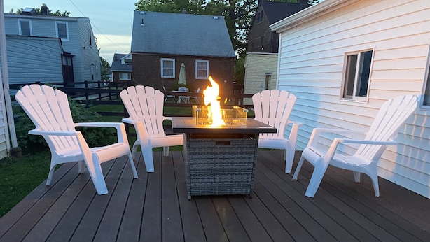 Une terrasse agrémentée d’un foyer et de chaises Adirondack blanches.