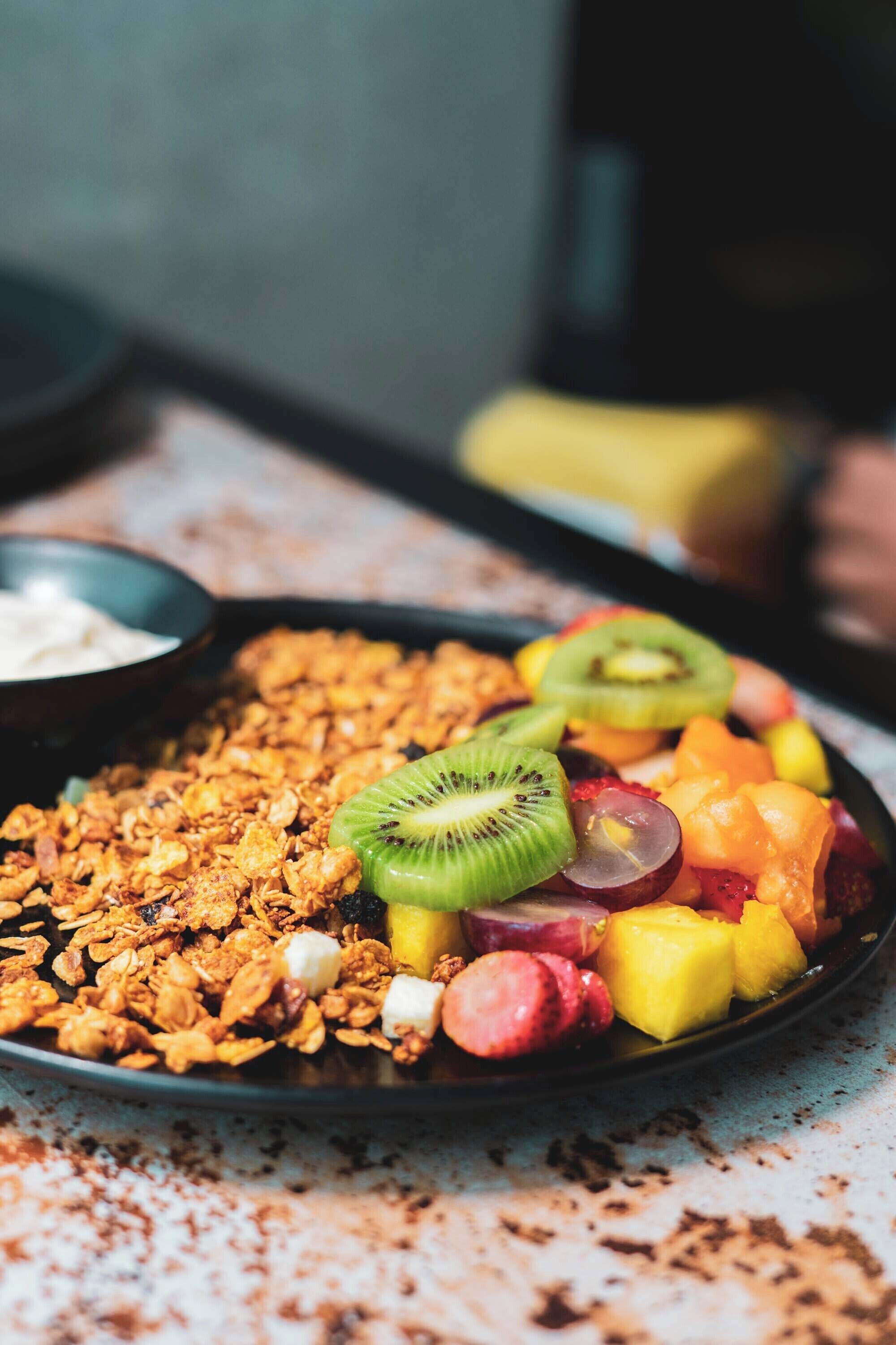 A plate of granola with various fruits and a small bowl of yogurt.