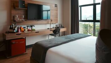A hotel room with a bed, a desk with a TV, a chair, and a window with a view.