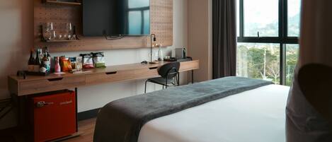 Una habitación de hotel con una cama, un escritorio con televisor, una silla y ventana con vistas.