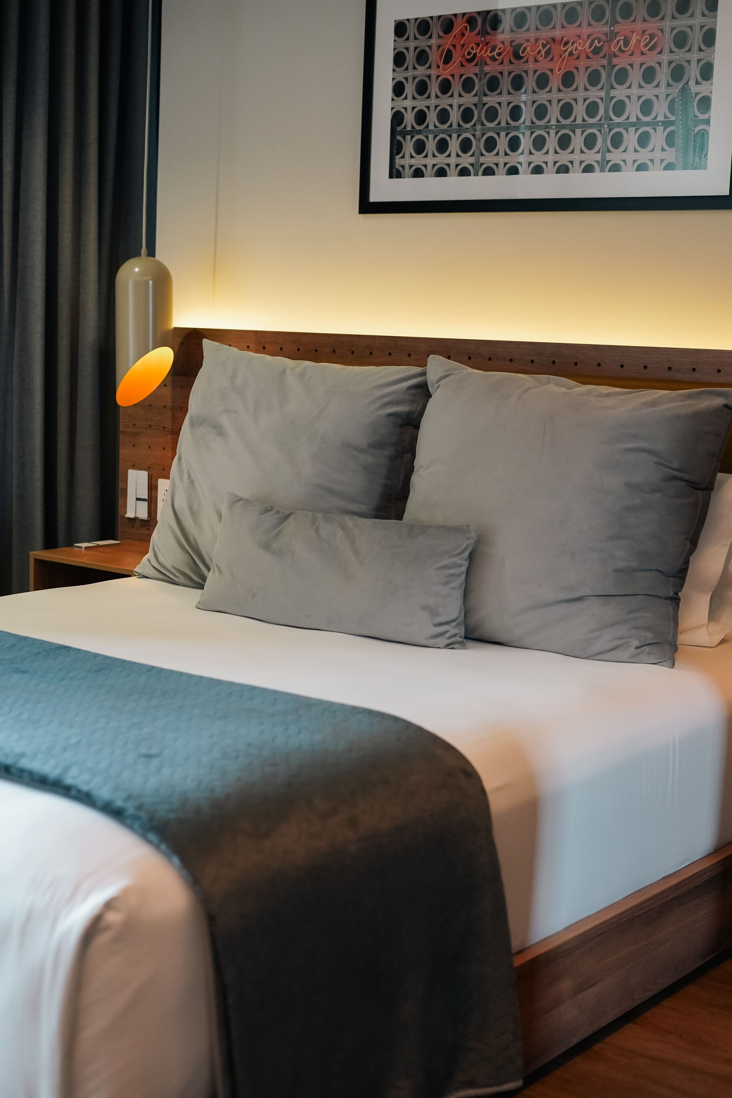 A neatly made bed with grey bedding and a wooden headboard.