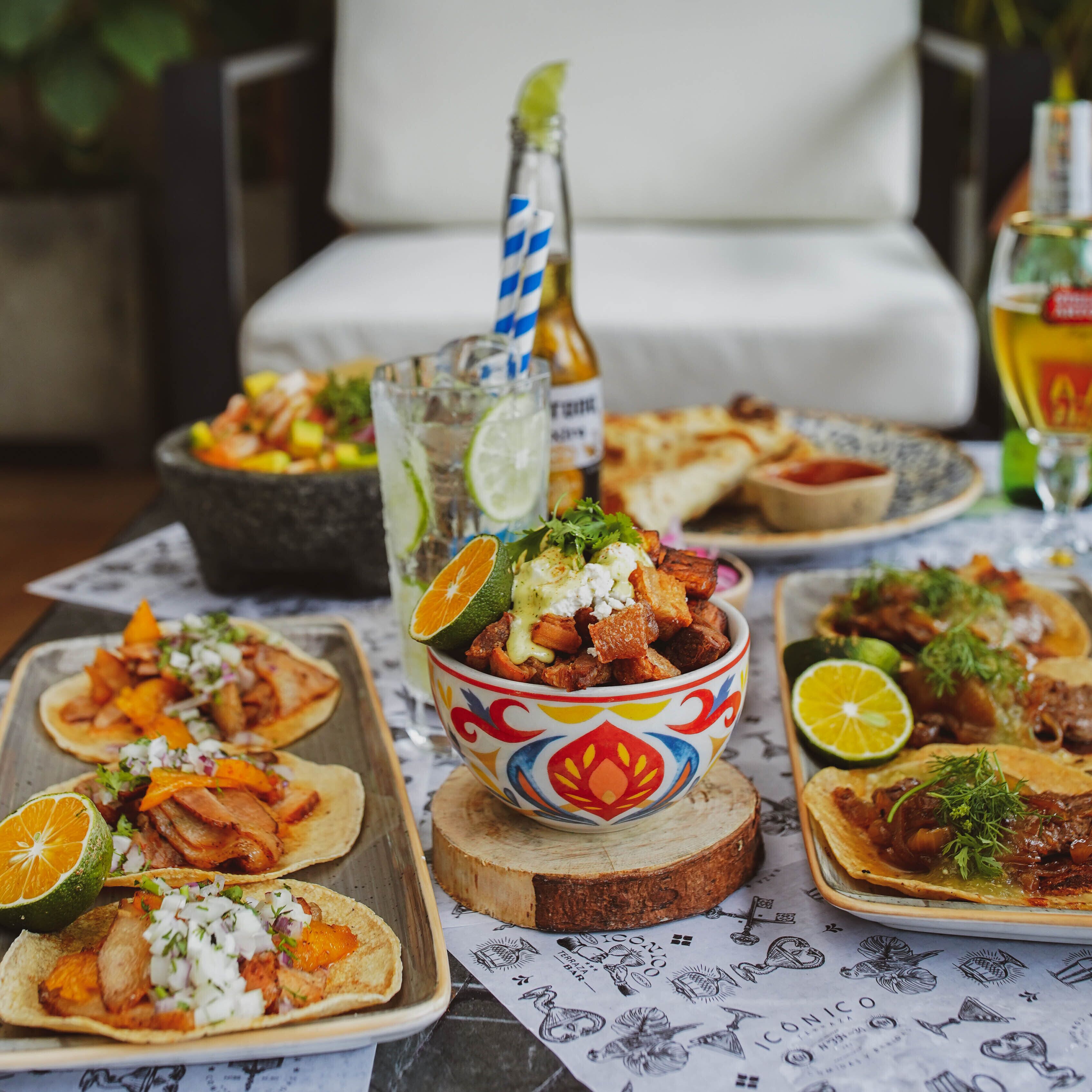 A table with various dishes, including tacos and a bowl of food, set on a table with a patterned tablecloth.