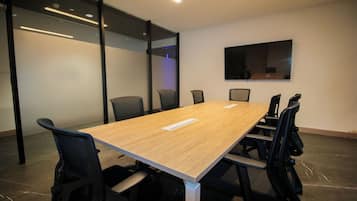 A conference room with a long table, black chairs, and a large flat-screen TV on the wall.
