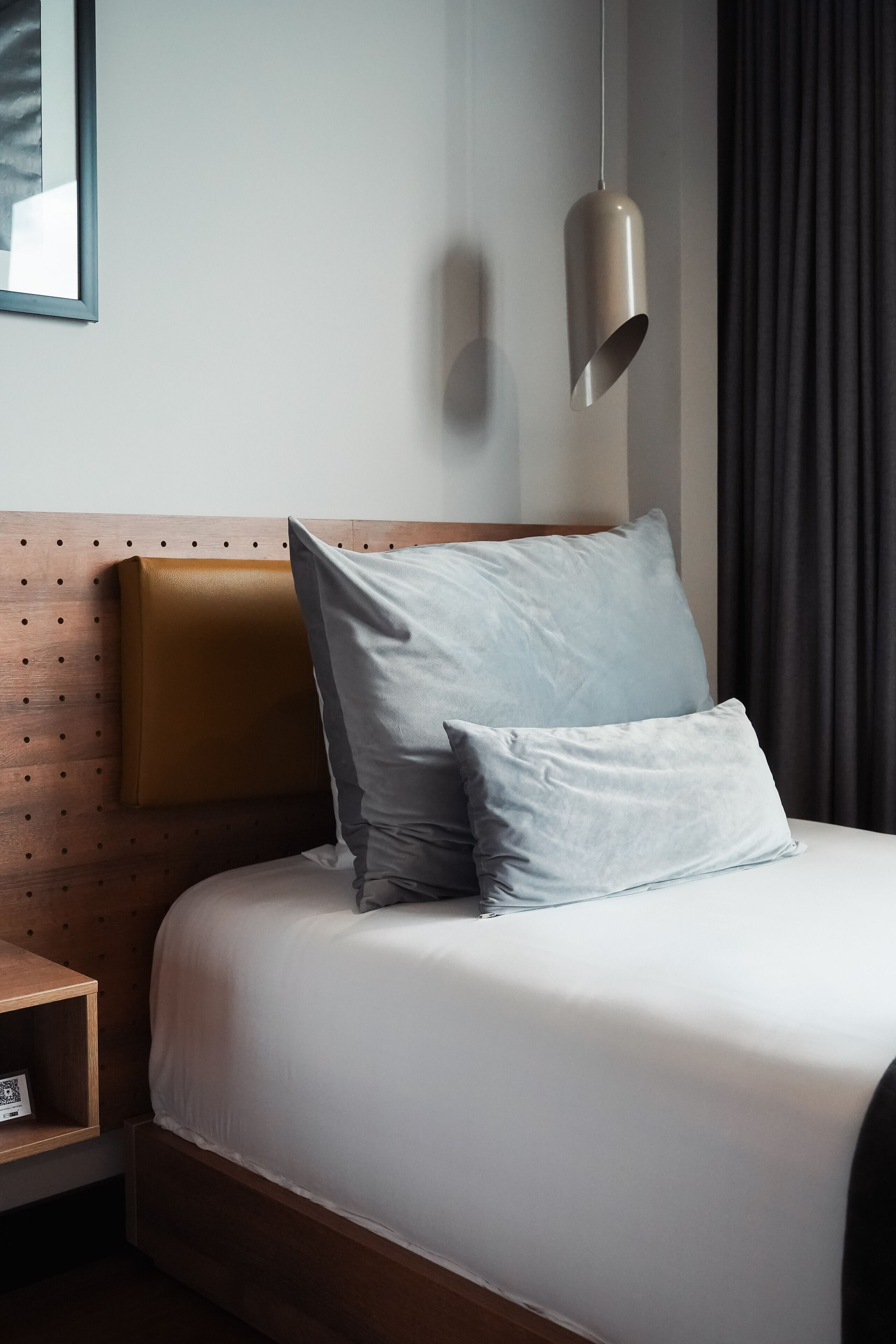 A neatly made bed with a wooden headboard, a bedside table with a book, and a pendant light.