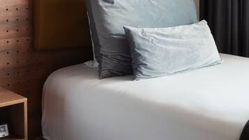A neatly made bed with a wooden headboard, a bedside table with a book, and a pendant light.