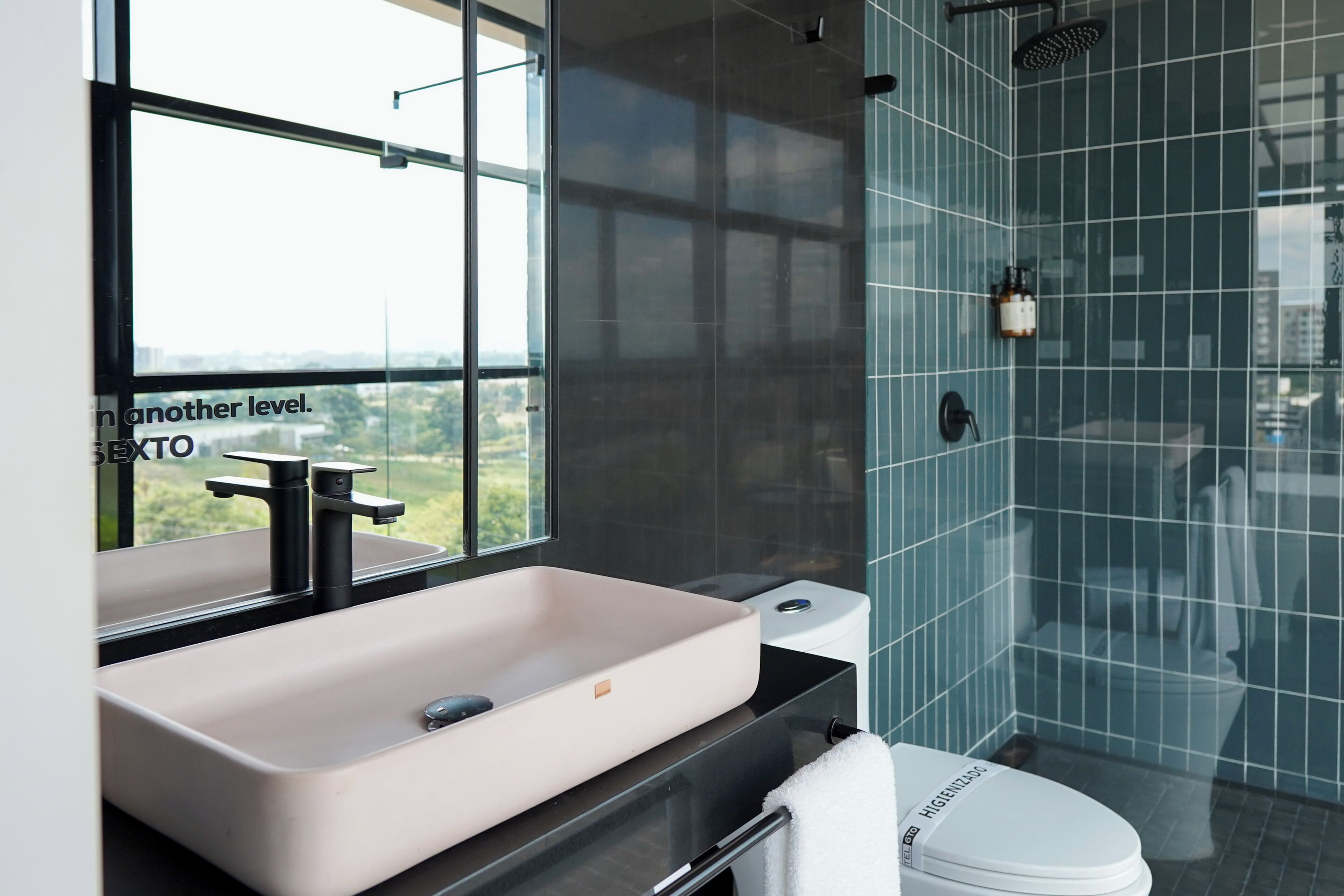Un baño moderno con un ventanal grande, un lavamanos color beige y un inodoro blanco.