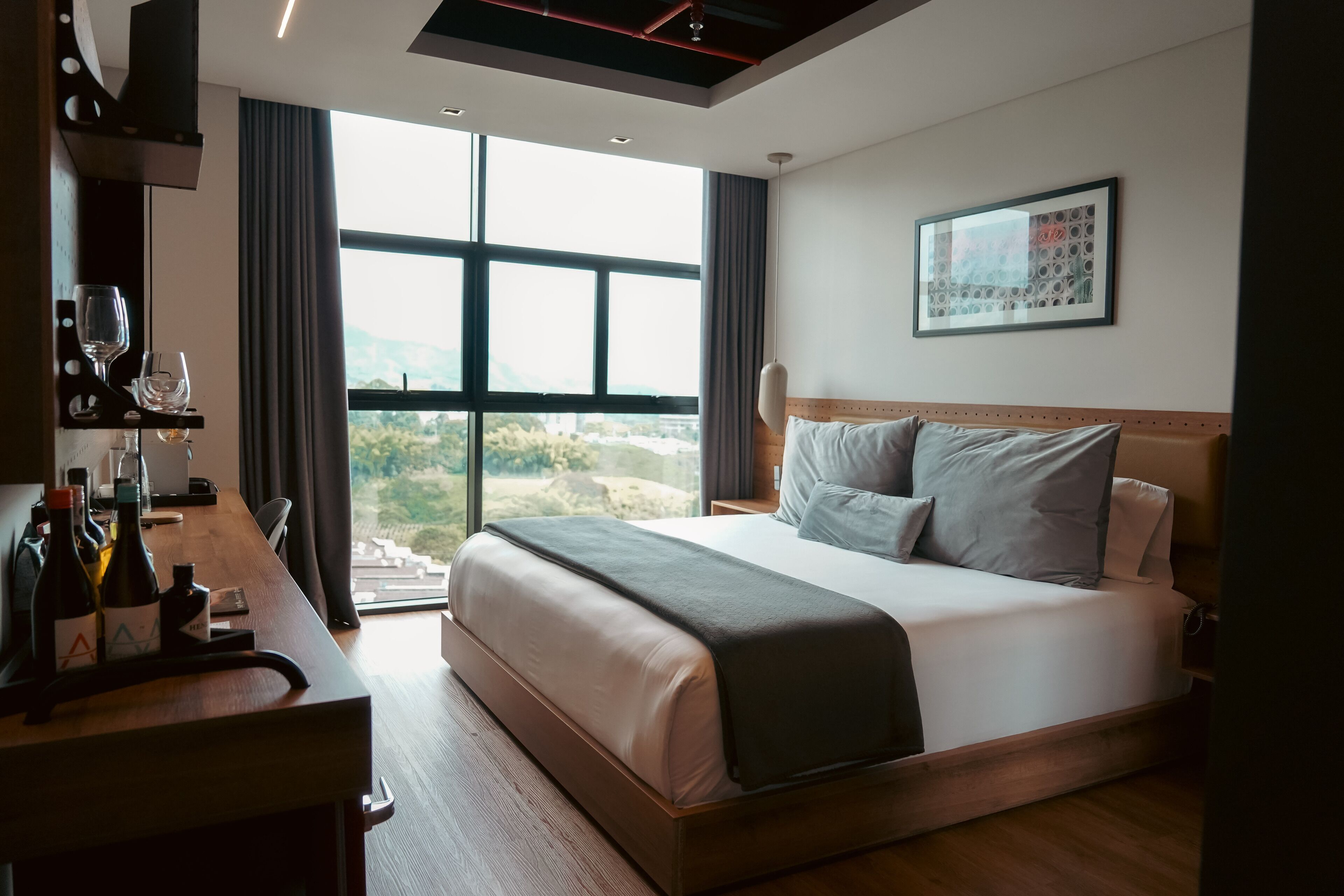 Quarto de hotel moderno com uma cama grande, uma mesa com garrafas de vinho e vista para o exterior.
