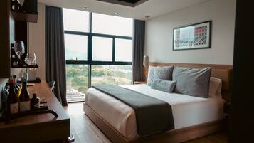 Quarto de hotel moderno com uma cama grande, uma mesa com garrafas de vinho e vista para o exterior.