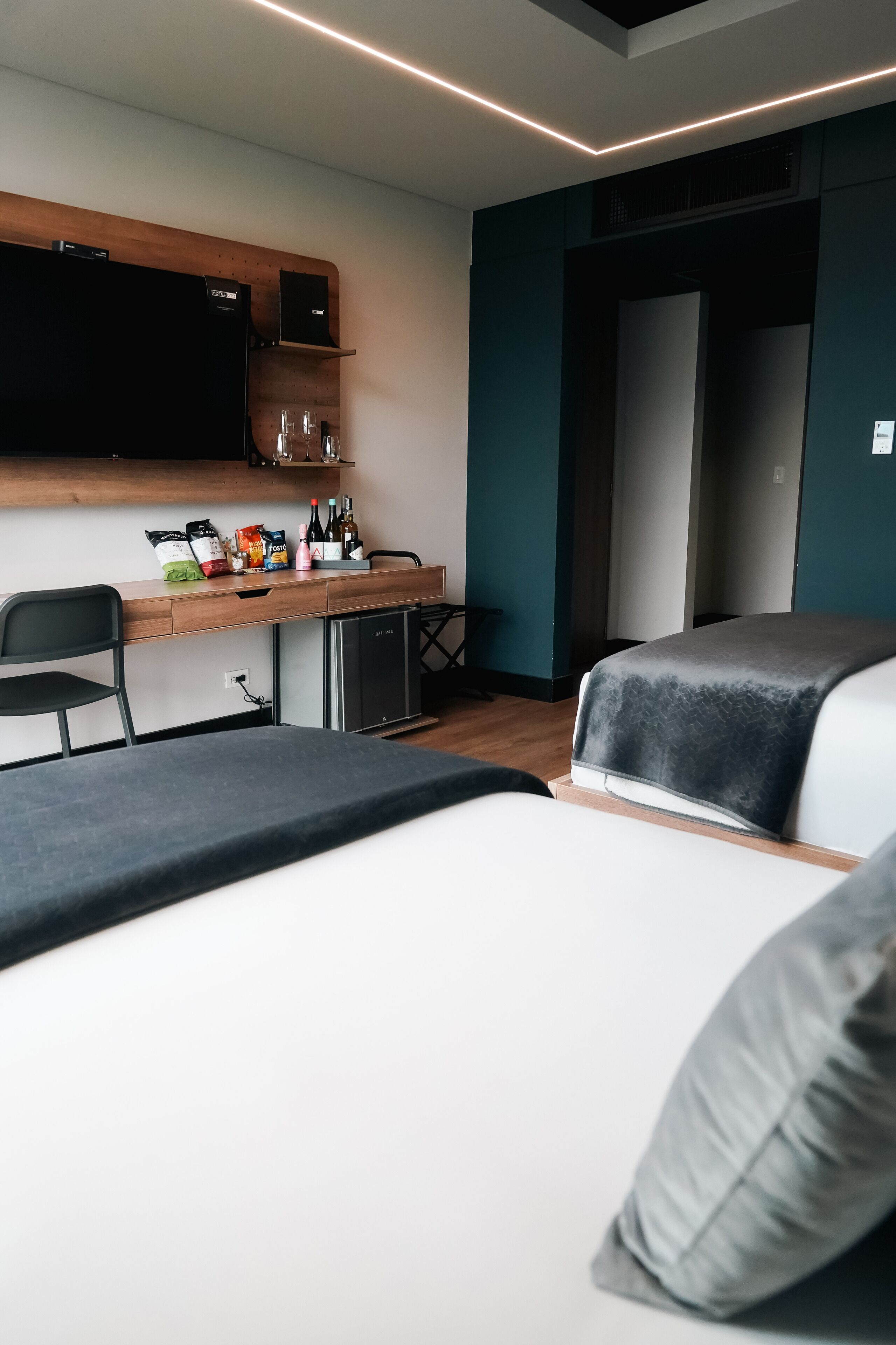 A modern hotel room with a bed, a desk with a computer, and a TV mounted on the wall.