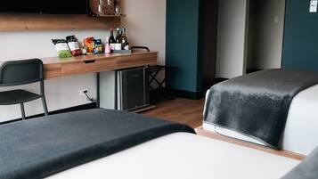 A modern hotel room with a bed, a desk with a computer, and a TV mounted on the wall.