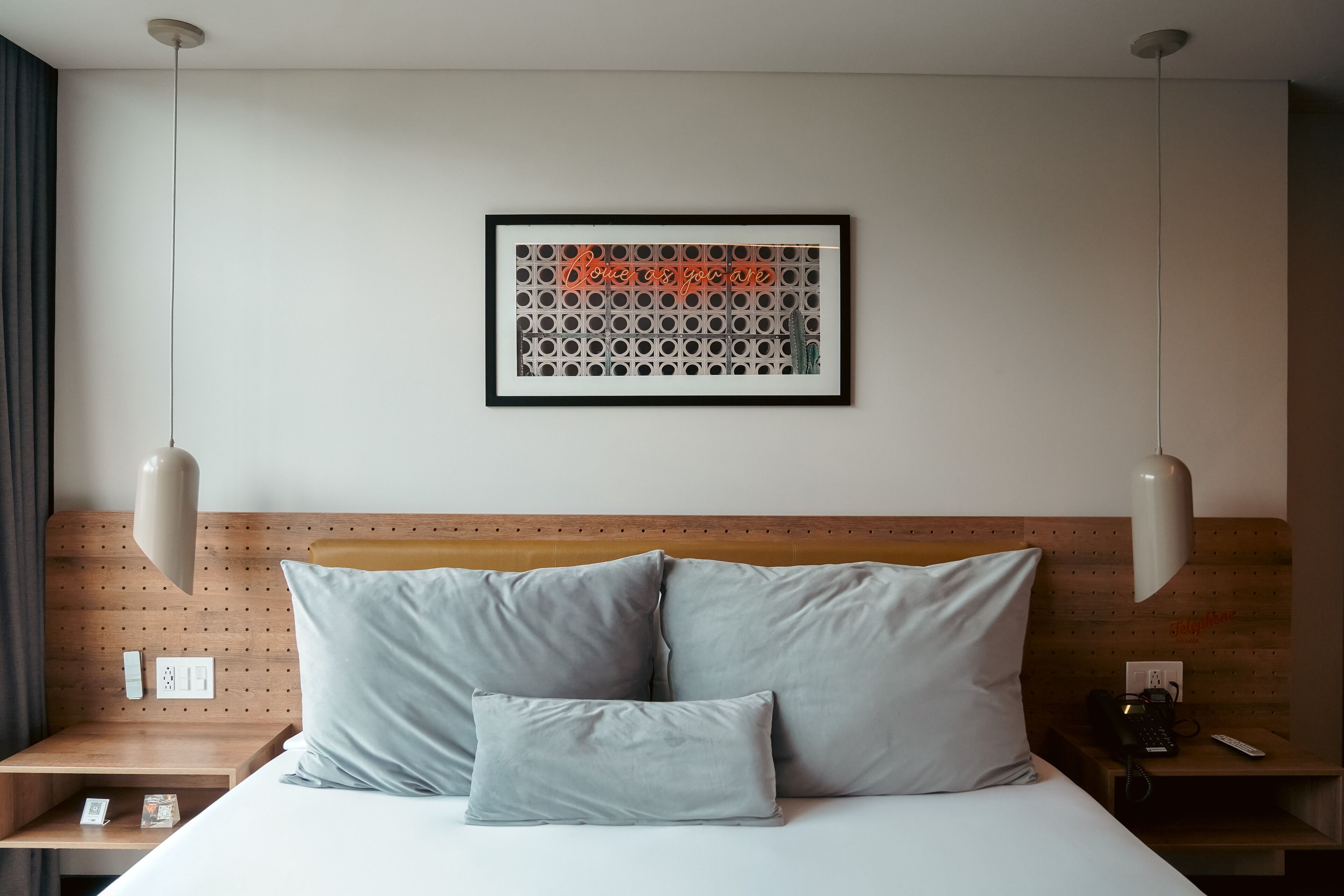 Una habitación de hotel con una cama, dos mesitas de noche, una obra de arte en la pared y una lámpara en el techo.