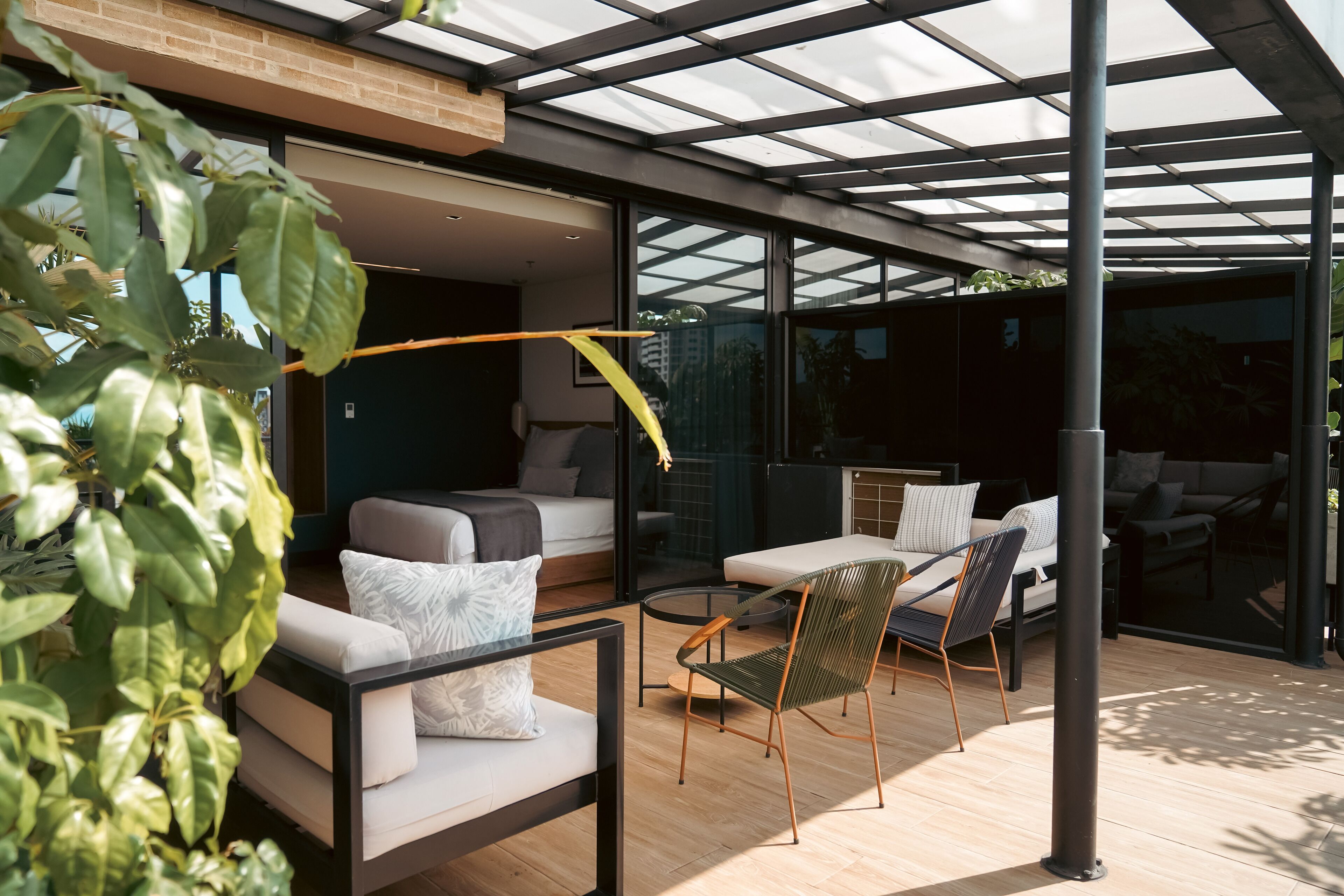 Un espacio exterior moderno con cerramiento de vidrio, un sofá, una silla y una mesa de comedor.