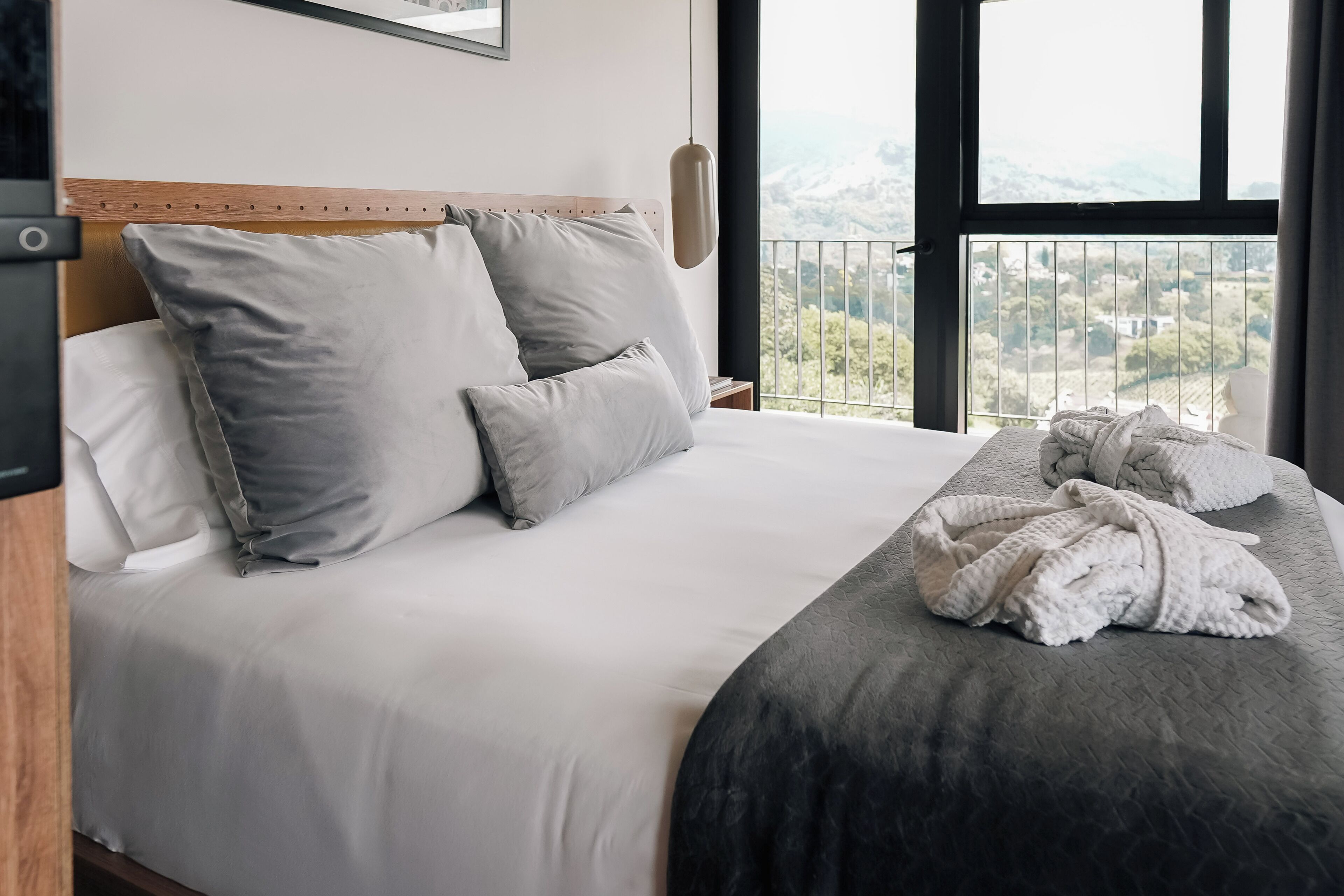 A hotel room with a bed, pillows, a blanket, and a view of the outdoors.