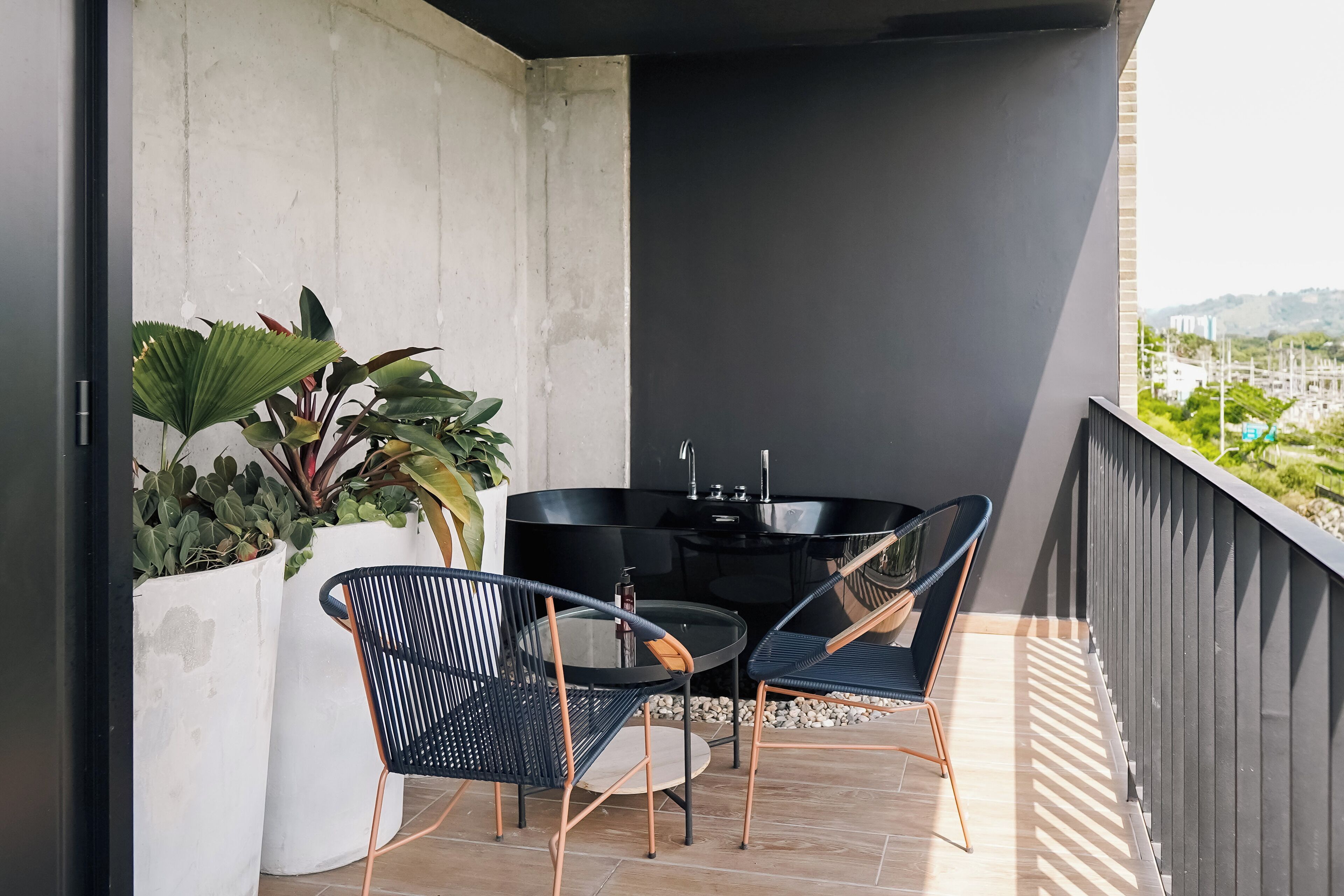 A balcony with a black table and chairs, potted plants, and a view of the city.