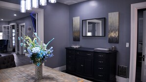 Un coin repas avec une table en bois, un vase de fleurs, un meuble noir et un miroir au mur.