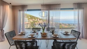 Un comedor con una mesa dispuesta para cuatro personas, un jarrón de flores y vistas a un pueblo costero.