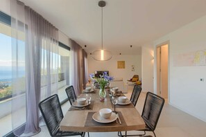 A dining area with a table set for four, a vase of flowers, and a view of the sea through large windows. - Amazing modern 3-BR villa with heated pool just above Icici Marina (Ičići)