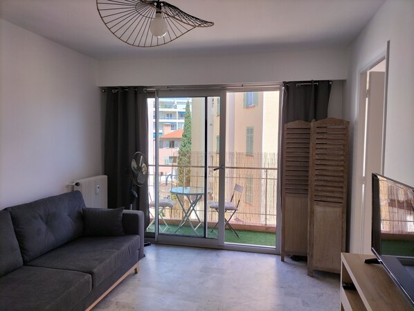 A modern living room with a grey sofa, a ceiling fan, a wooden cabinet, and a TV on a wooden stand.