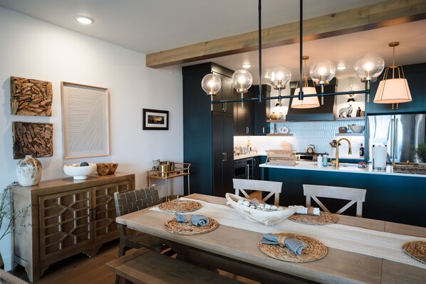 A modern kitchen with dark cabinetry, a central island, and pendant lighting. - Water View & Perfect Location at Shore View — Walk to Town, Beach & Marina! (Sister Bay)