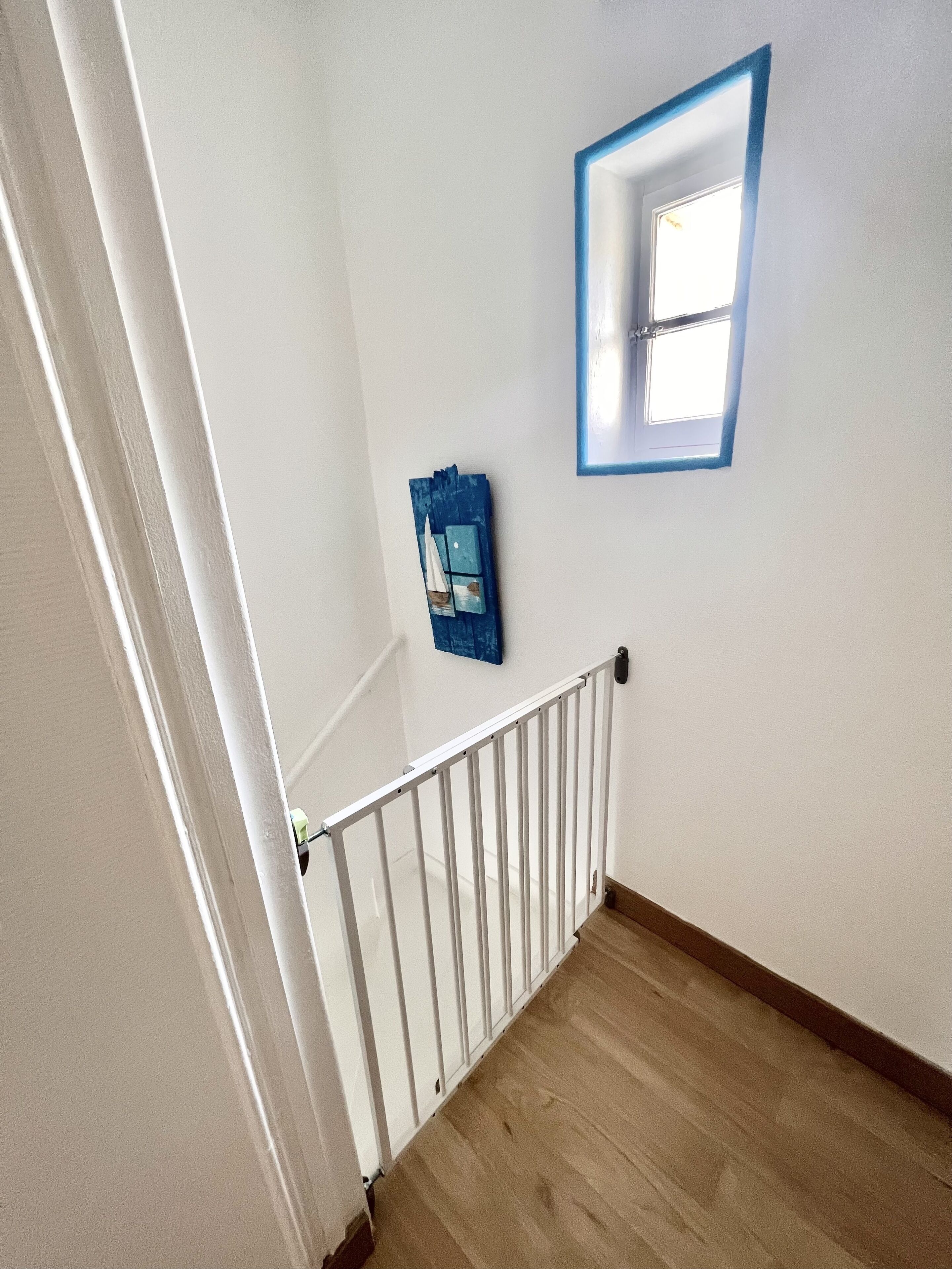 A staircase with a white railing, a wooden floor, and a small window with a blue frame.