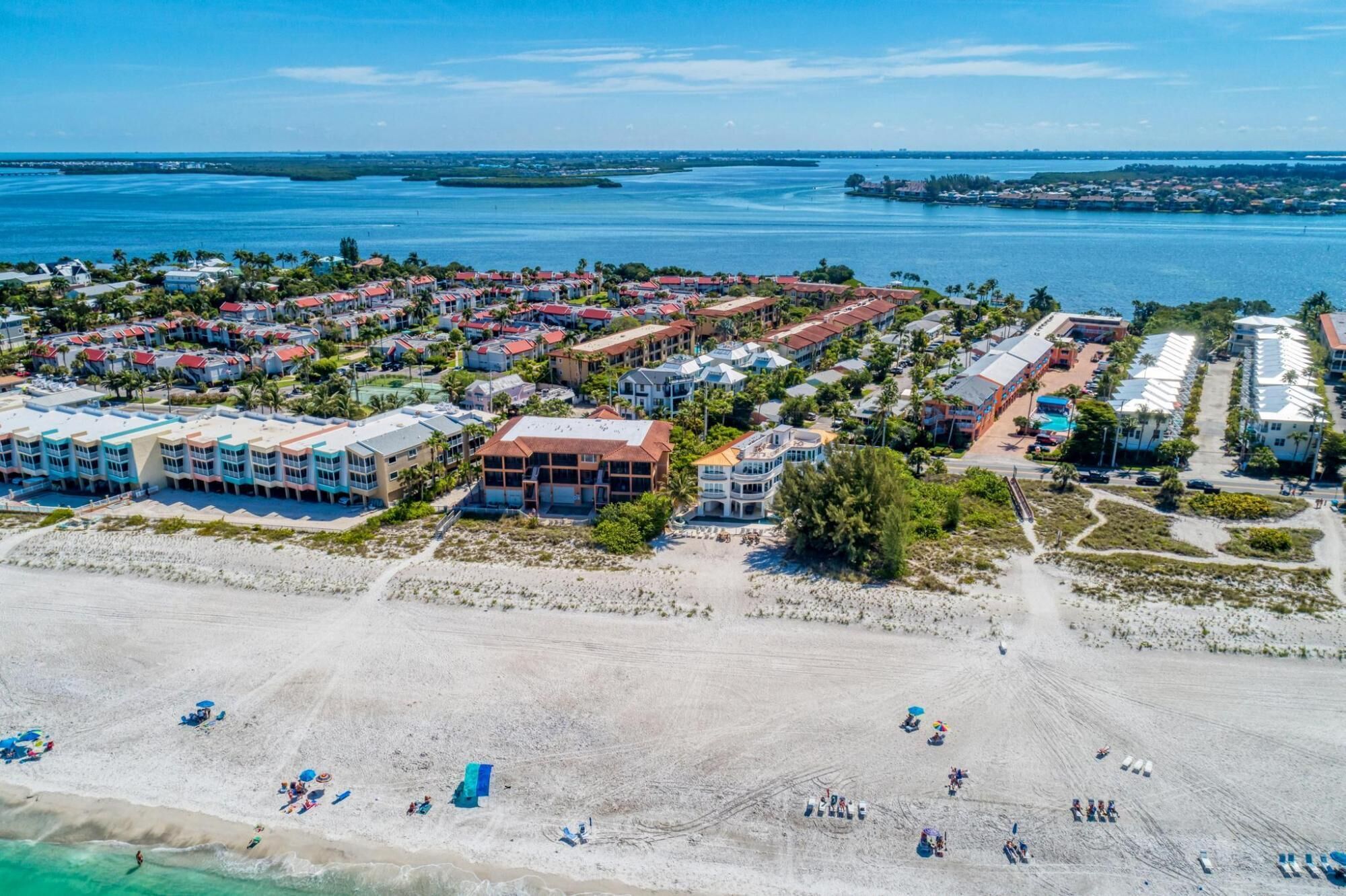 Vista aérea de um resort à beira-mar, com vários edifícios, uma praia de areia e um porto de iates.