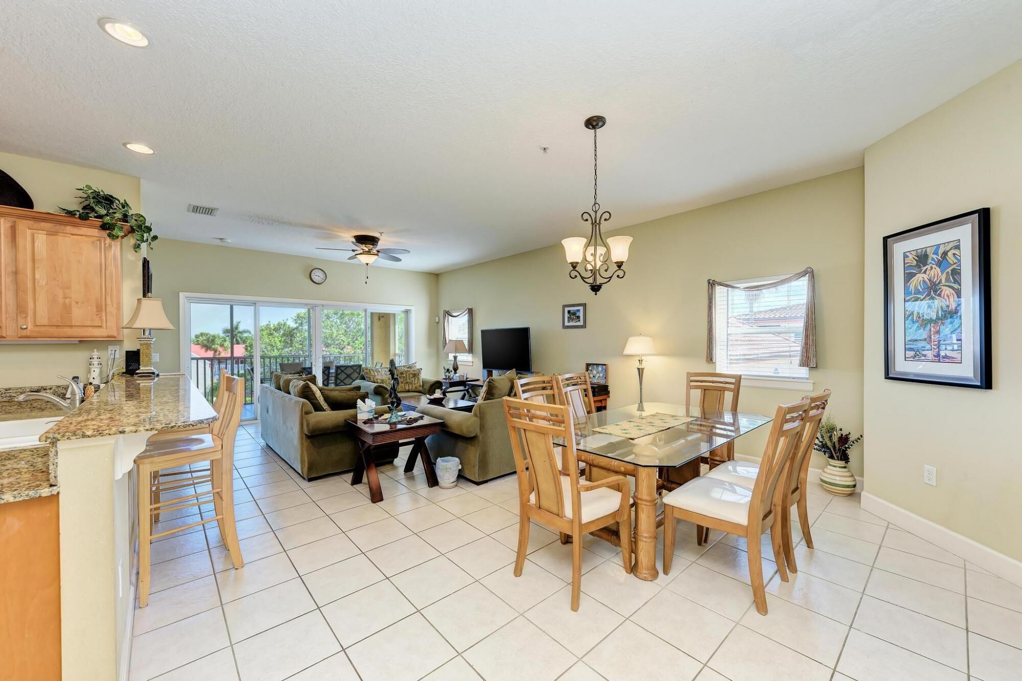 A spacious living area with a dining table, chairs, and a kitchen area with wooden cabinets and a granite countertop.