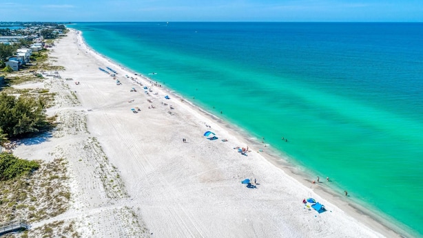 An aerial view of a beach with clear turquoise waters, a sandy shore, and a row of beach umbrellas. - Bradenton Beach Club Bliss-2 Bedroom-2 Bathroom Condo-2 Pools-hottub-private Beach Access (Bradenton Beach)