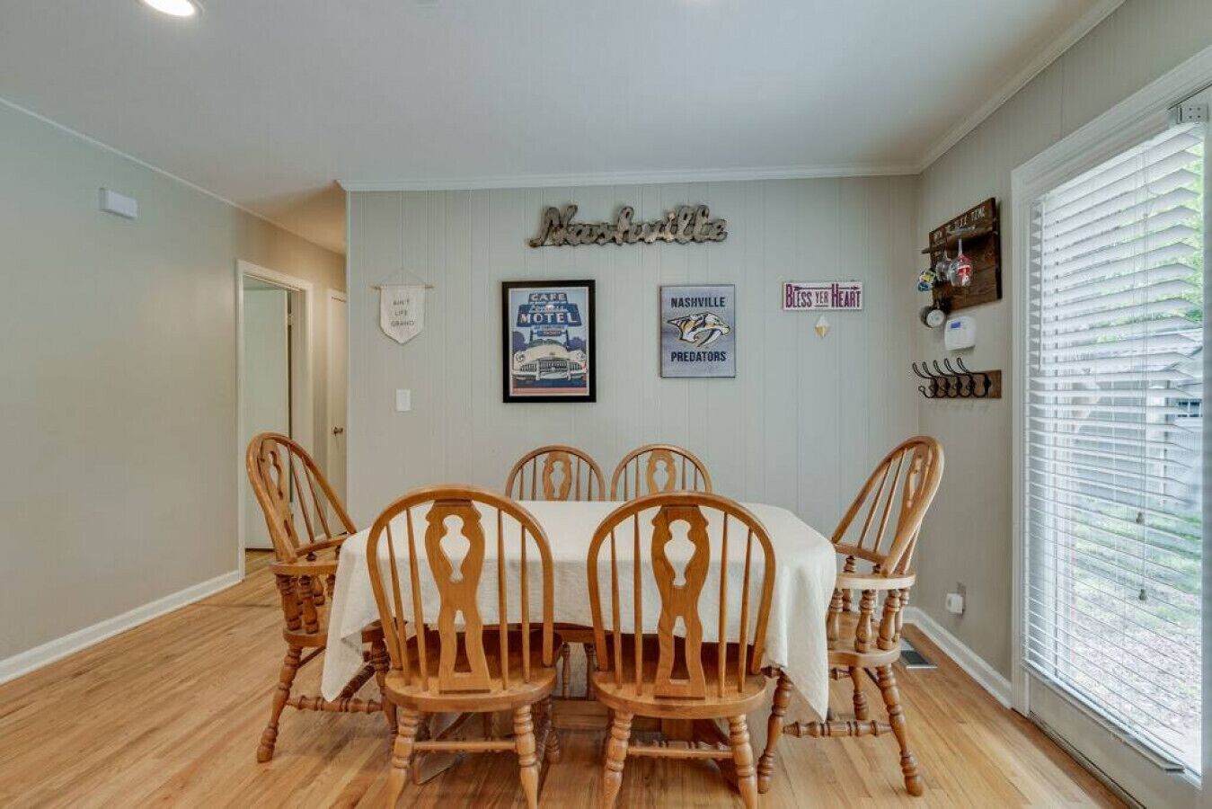 Un comedor con una mesa y sillas de madera, una pared adornada con marcos y una ventana con persianas.