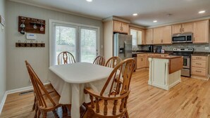 A kitchen with wooden cabinets, a refrigerator, a microwave, and a stove. There is a dining table with chairs and a window with blinds. - Casa Rover - Pet Friendly w/ Fenced-in Yard, Family Friendly, Mins to Downtown Nashville (Nashville)