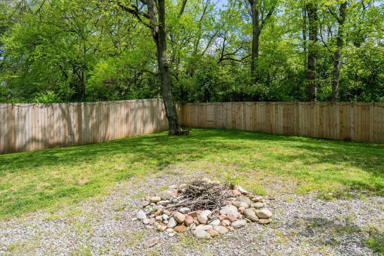 A backyard with a fire pit surrounded by rocks and a wooden fence.