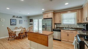 A modern kitchen with wooden cabinets, a stainless steel refrigerator, and a dining area with a wooden table and chairs. - Casa Rover - Pet Friendly w/ Fenced-in Yard, Family Friendly, Mins to Downtown Nashville (Nashville)