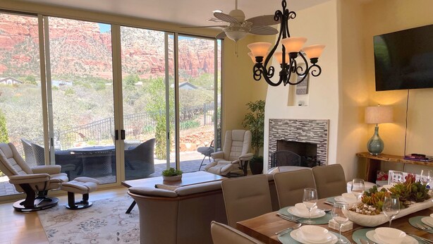 Comedor con una mesa grande dispuesta para seis personas, chimenea y vistas a formaciones rocosas rojas a través de puertas correderas grandes.