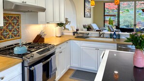 Una cocina moderna con armarios blancos, estufa a gas y lavavajillas. Hay una ventana que ofrece vistas a un paisaje rojo.