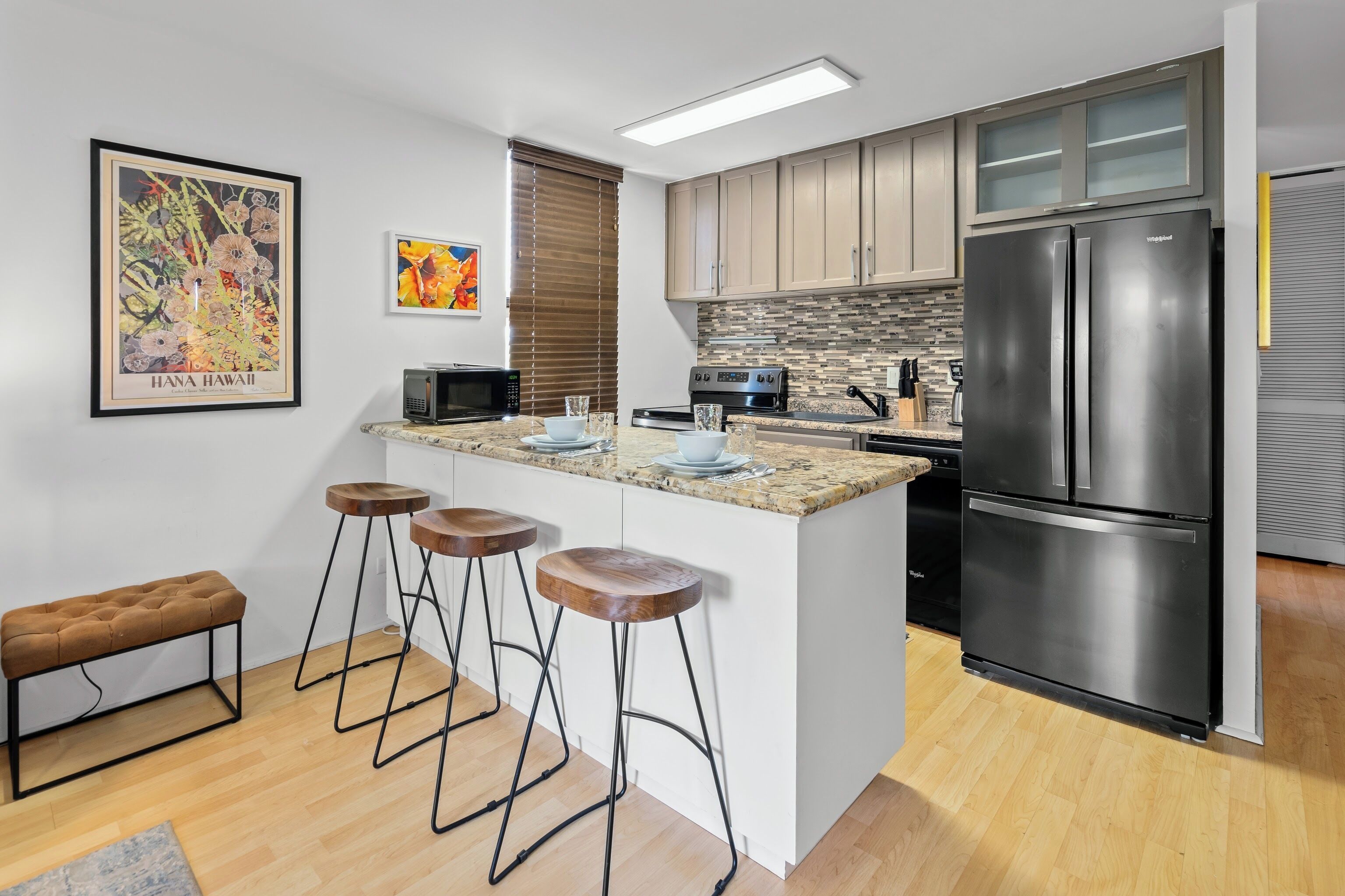 A modern kitchen with a central island, bar stools, a refrigerator, and a microwave.