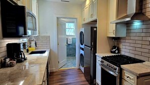 A kitchen with a stove, microwave, refrigerator, and a washing machine in the background.
