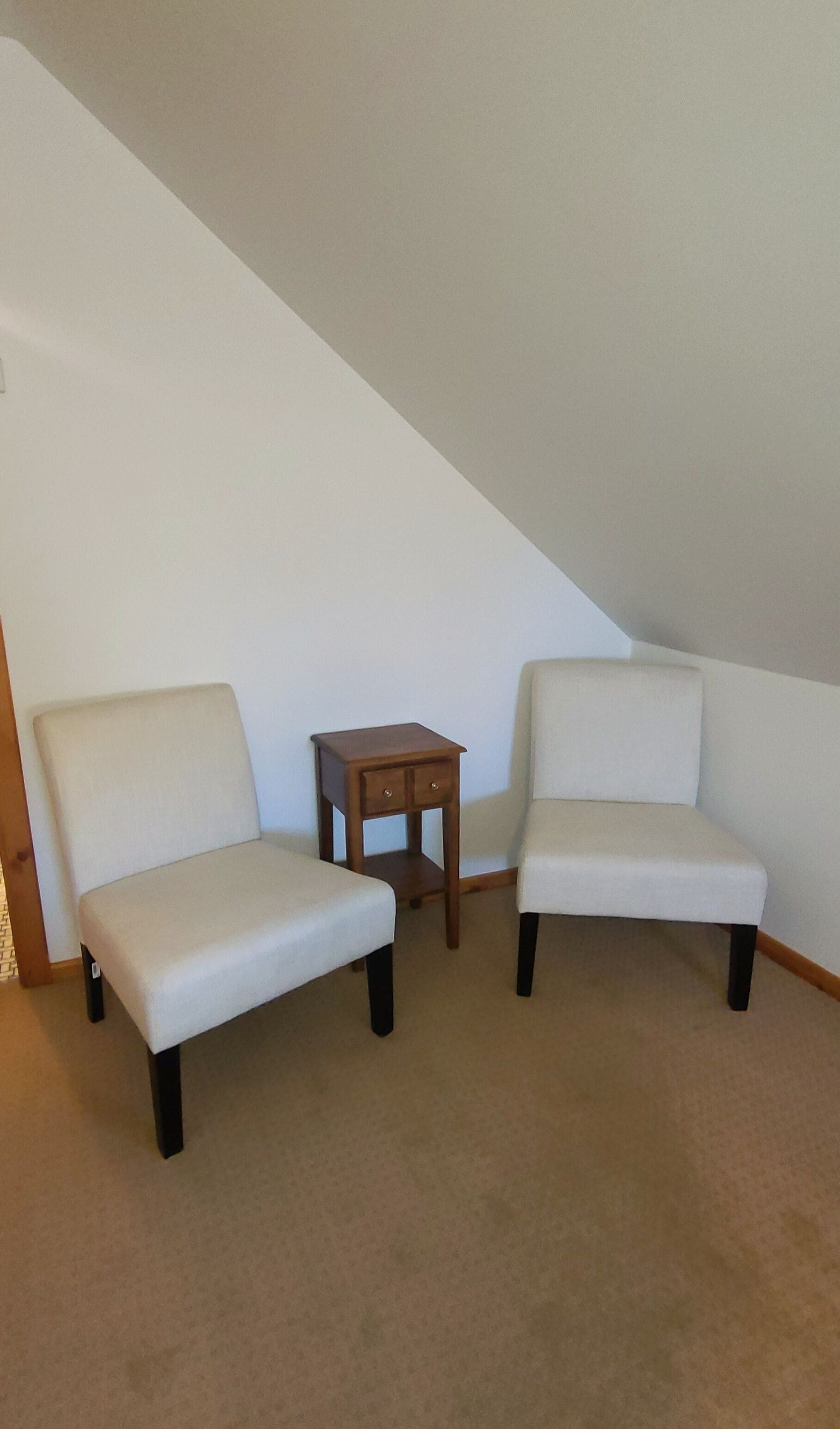 Une pièce avec deux fauteuils blancs et une petite table d’appoint en bois.