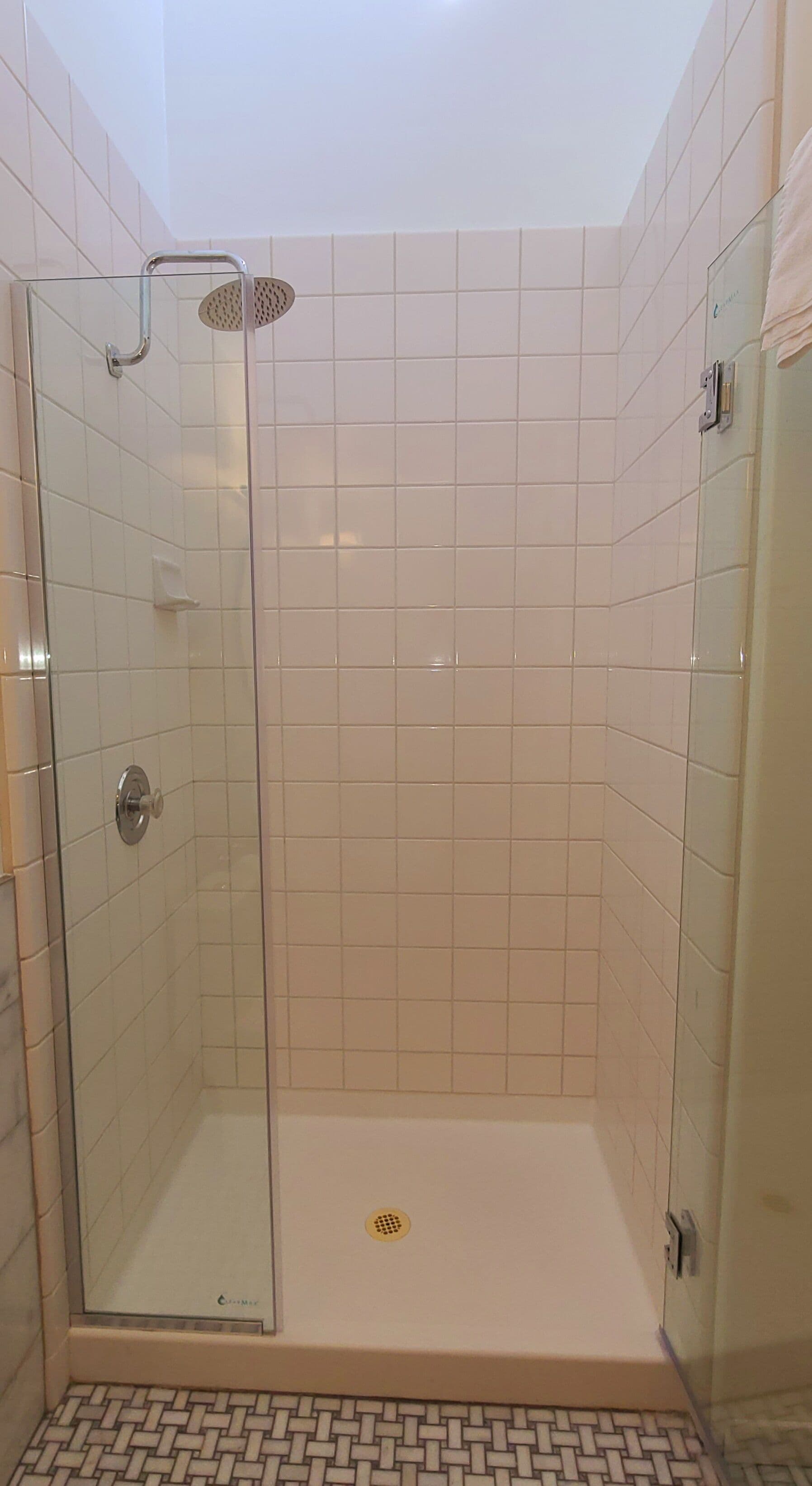 A glass-enclosed shower with a handheld showerhead, tiled walls, and a patterned floor.