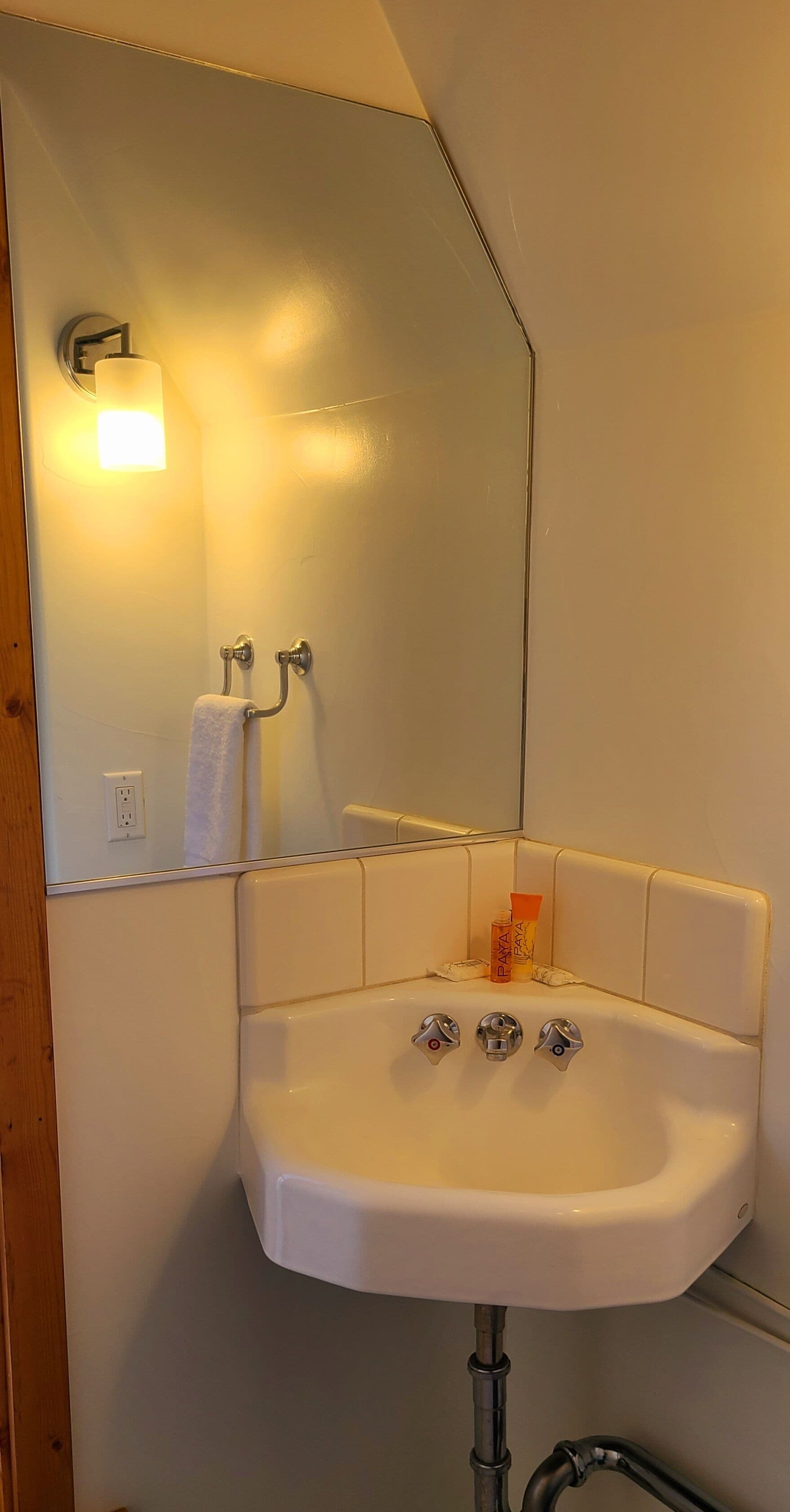 A bathroom with a white sink, a mirror, a towel rack, and a soap dispenser.