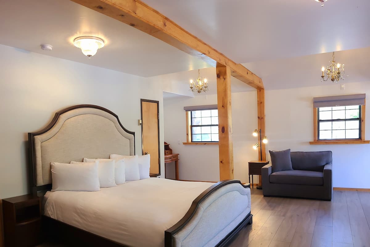 Quarto com cama grande, vigas de madeira, sofá e duas janelas.