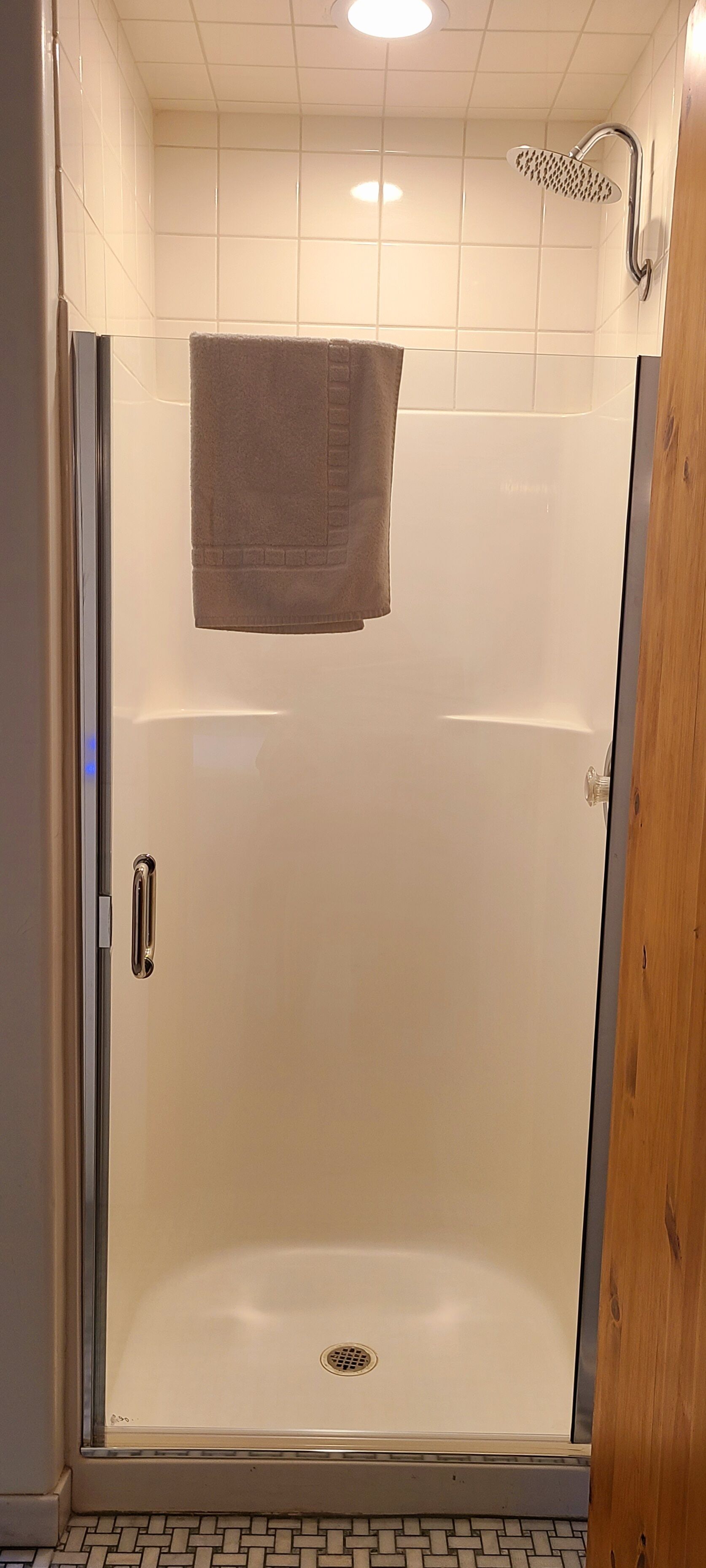 A walk-in shower with a glass door, a towel hanging on the wall, and a tiled floor.