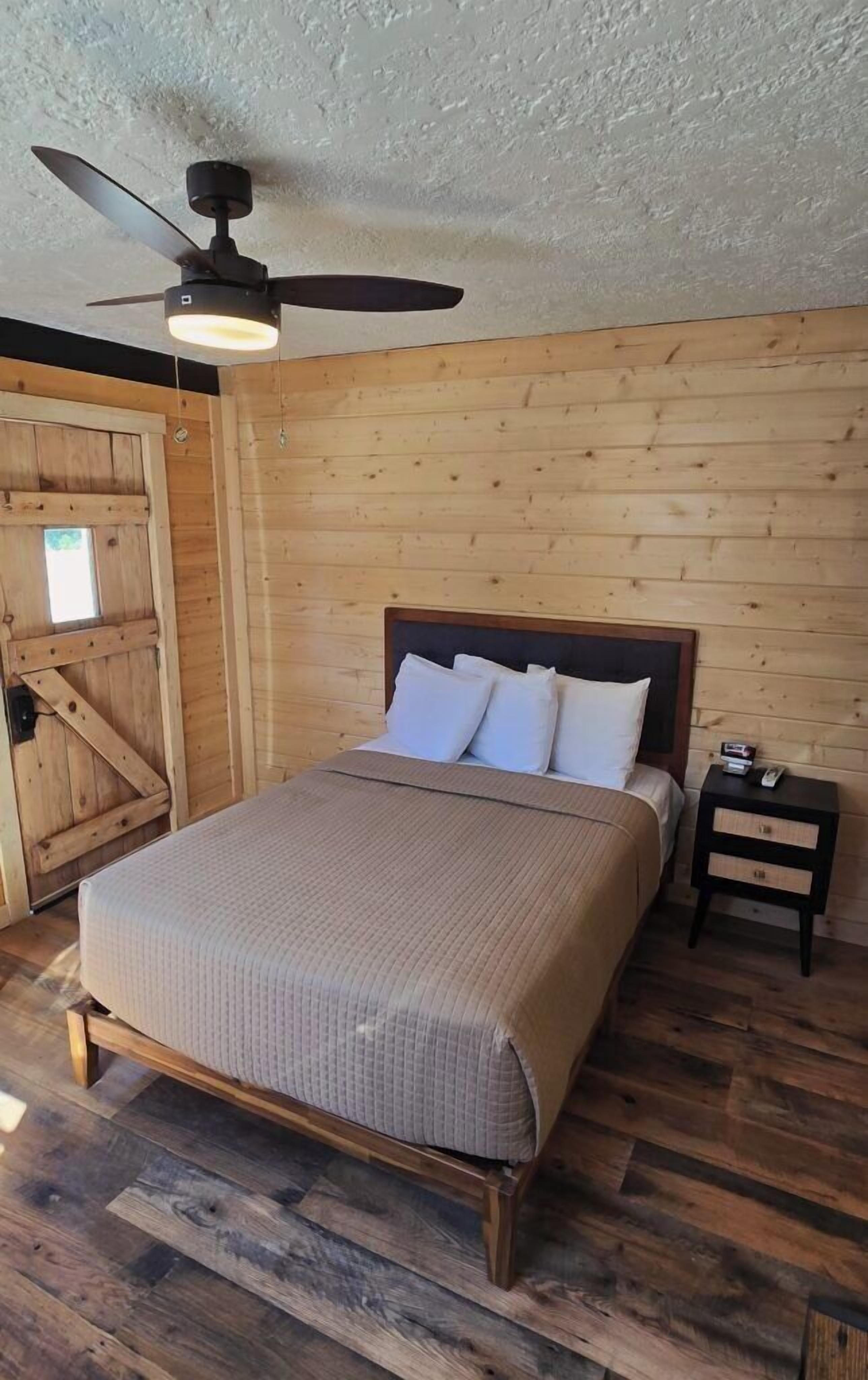 A wooden-paneled room with a bed, a nightstand, and a ceiling fan.