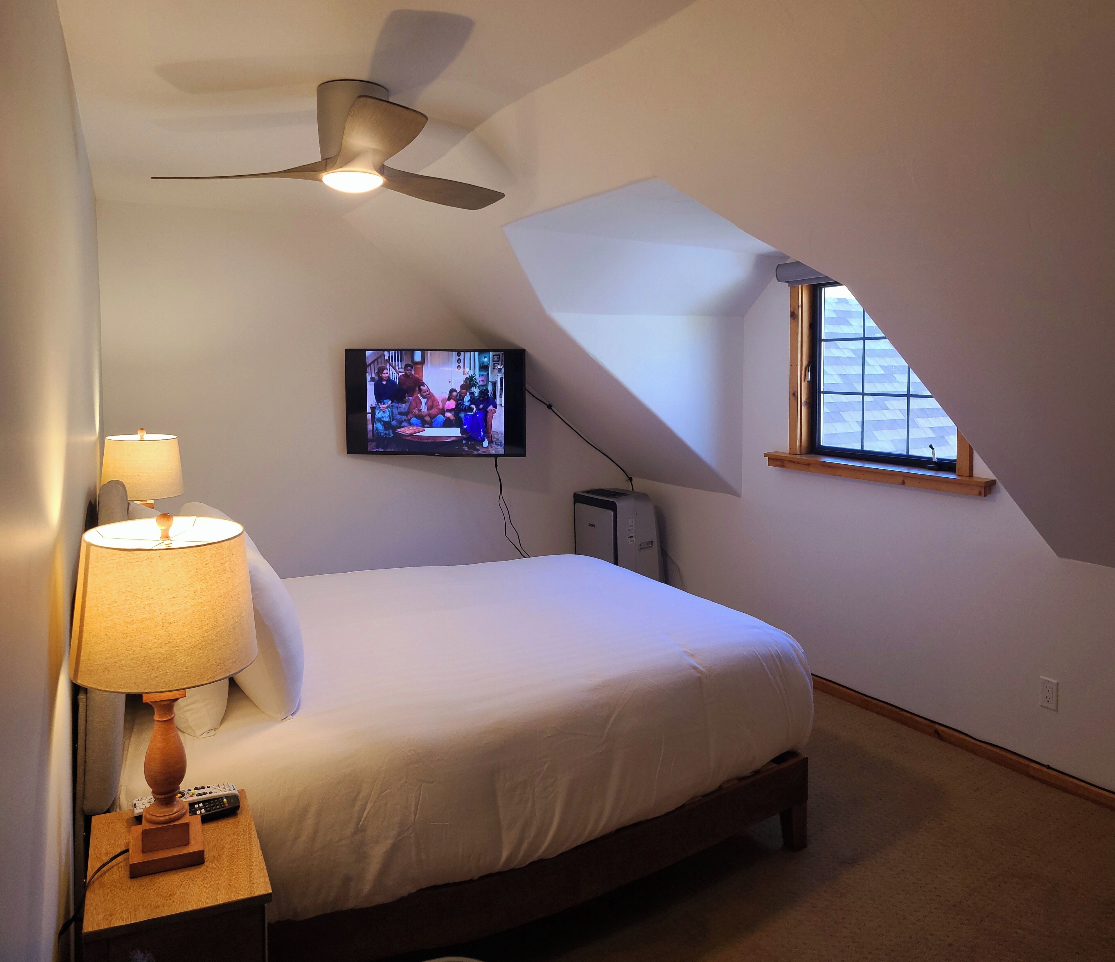 Une chambre à coucher avec un lit, un ventilateur de plafond, une télévision, une lampe et une fenêtre.