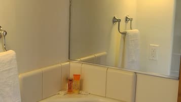 Un baño con un lavamanos blanco, dos llaves, un espejo y un perchero para toallas.
