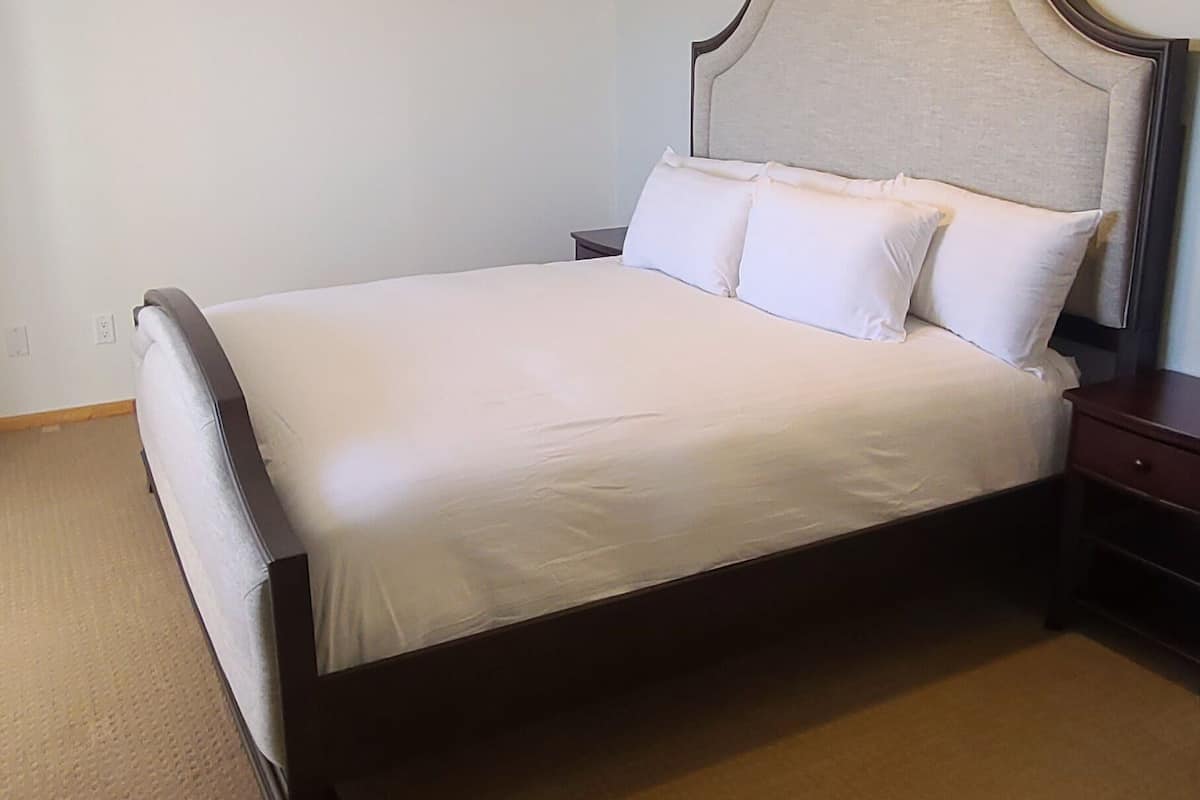 Quarto com cama, mesa de cabeceira, ventoinha no teto e piso coberto por carpete.