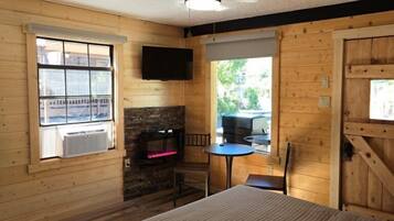 A cozy cabin room with a bed, a stone fireplace, a TV, and a window overlooking a deck.