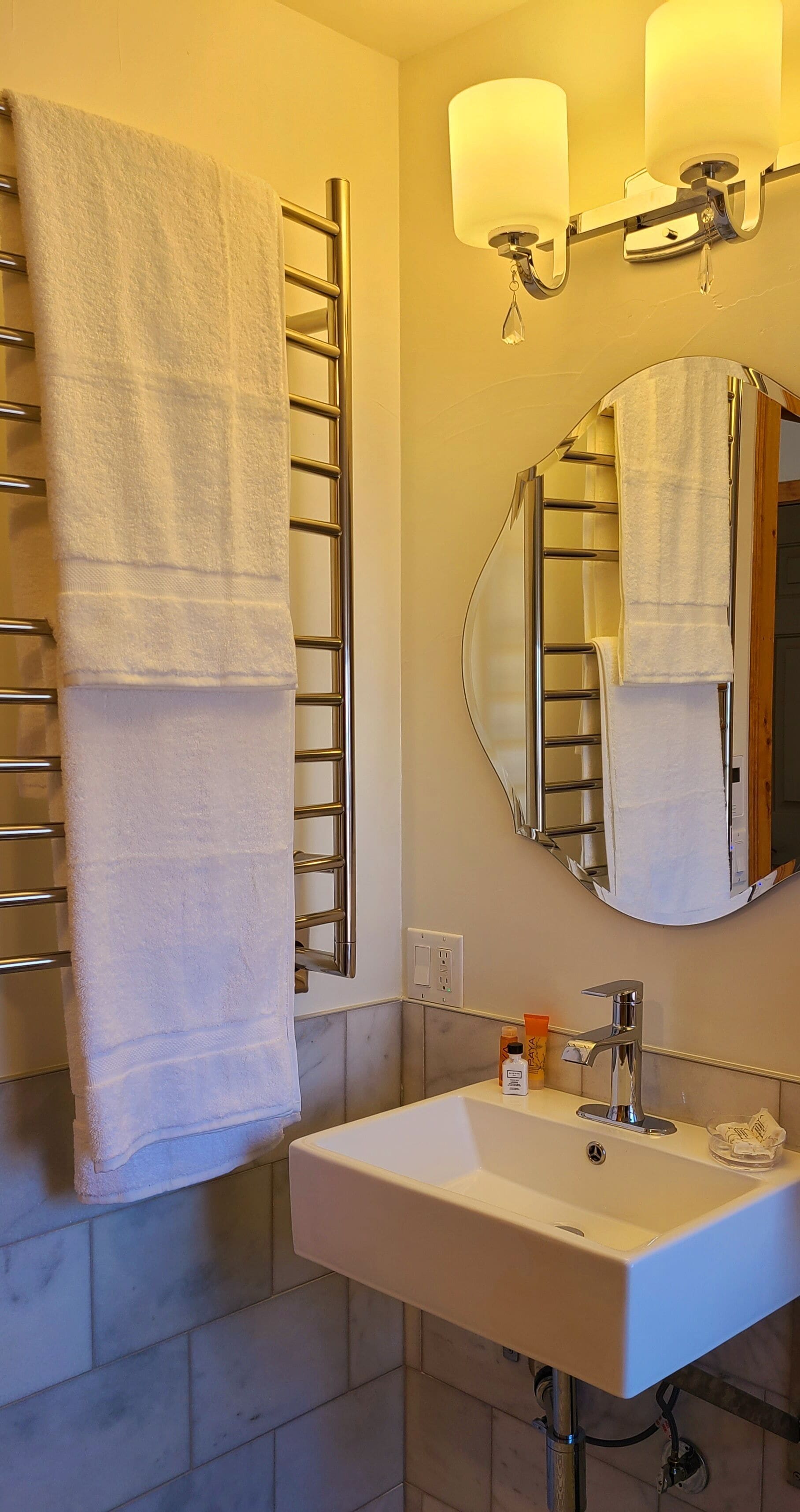 Une salle de bain avec un lavabo blanc, un miroir et un porte-serviettes sur lequel est accrochée une serviette.