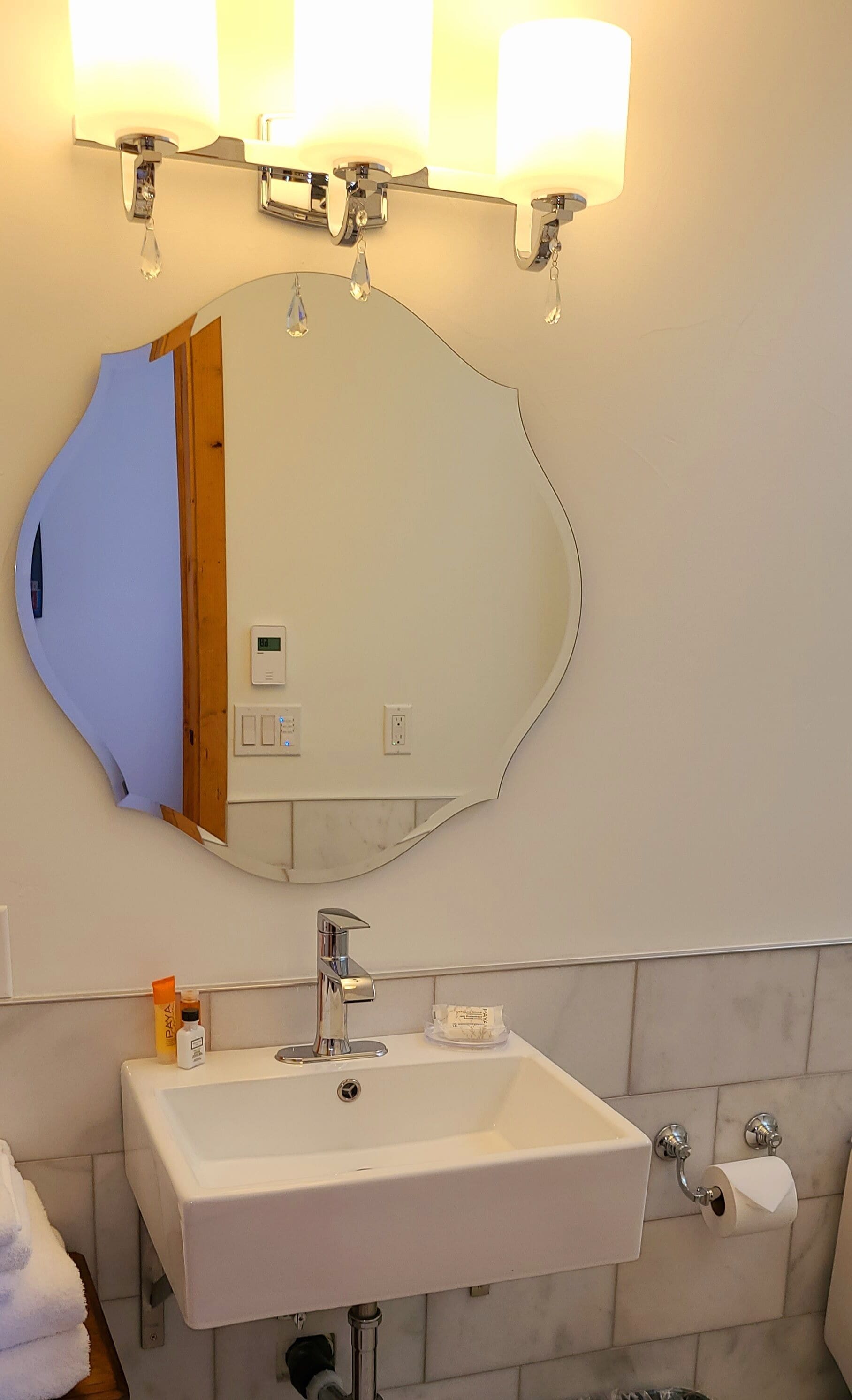 Un baño con un lavabo blanco, un espejo y tres luces instaladas en la pared.